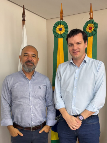 O representante da CEASA/RS junto ao representante da AGAS, posam para foto em frente a bandeiras com fitas verdes e amarelas. Ambos usam camisas sociais claras e sorriem levemente para a c&acirc;mera